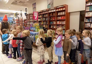 Dzieci stoją w rzędzie jedno za drugim ustawione przed mężczyzną w czapce krasnala.