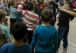 Chłopcy stojący tyłem noszą zgiętą jedną rękę w górą – naśladują tancerkę.