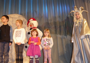 Na scenie stoi czwórka dzieci. Obok nich stoją aktorzy w strojach bałwana i Królowej Zimy
