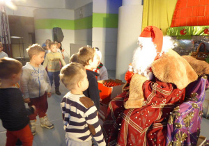 Chłopcy stoją przed Mikołajem, który w ręku trzyma czekoladową figurkę Mikołaja.