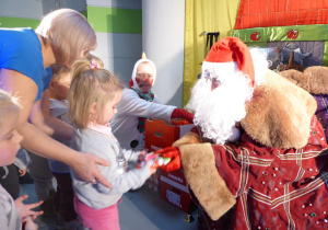 Mikołaj podaje dziewczynce czekoladową figurkę.