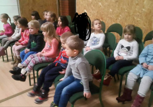 Dzieci siedzą na krzesłach i patrzą w jednym kierunku.