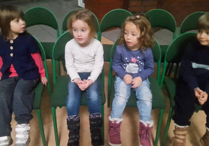 Zbliżenie na czwórkę dzieci siedzących na krzesłach – trzy dziewczynki i jeden chłopiec.