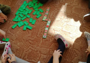 Dzieci siedząc na podłodze grają w kolorowe domino obrazkowe
