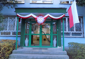 Drzwi wejściowe do przedszkola, ozdobione godłem Polski i biało-czerwonymi flagami