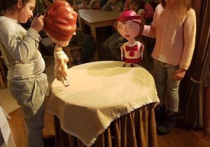 Dziewczynki stoją naprzeciw siebie i trzymają lalki Czerwonego Kapturka i mamy