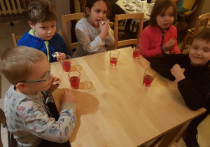 Dzieci przy stoliku jedzą ciasteczko i piją soczek