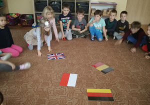 Dzieci siedzą na dywanie i rozpoznają flagę Polski wśród różnych flag
