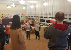 Dzieci z rodzicami stojąc w kręgu pokazują flagę Polski