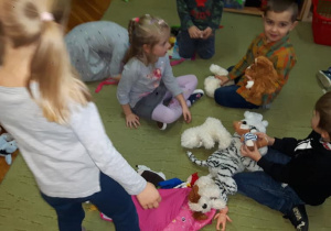 Dzieci siedzą na dywanie i oglądają pluszami
