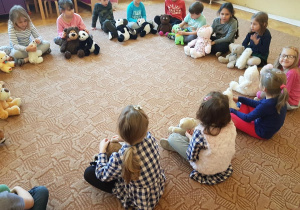 Dzieci siedzą w kręgu na dywanie ze swoimi misiami