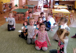Dzieci siedzą na dywanie i machają rękami
