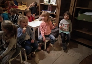 Dzieci siedzą przy stolikach i jedzą ciasteczko