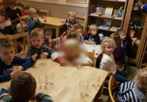 - Dzieci siedzą przy stolikach, piją soczek i jedzą ciasteczko