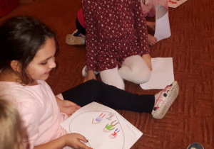 Dziewczynka siedząc na dywanie pokazuje swój rysunek