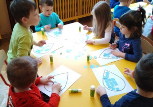 - Dzieci przyklejają niebieski papier na kartki z narysowanymi konturami kropli wody