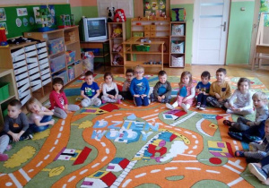 - Dzieci siedzą na dywanie w półokręgu