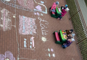 - Dzieci patrzą na laurkę dla Łodzi wykonaną przez siebie kolorową kredą na tarasie przedszkolnym
