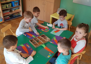 - Dzieci tworzą kompozycję marchewki na kolorowym tle z papieru i plasteliny