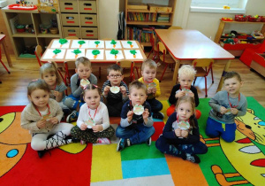 - Dzieci siedzą na dywanie i pokazują ordery z marchewką