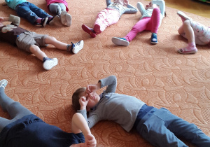 Dzieci leżą na dywanie. Odpoczywają. Zakrywają dłońmi oczy.