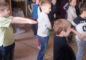 Grupa stojących chłopców ze złączonymi rękami wyciągniętymi do przodu lub ułożonymi na biodrze.