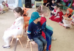 Pięcioro dzieci siedzi na krzesełkach ustawionych plecami do siebie.