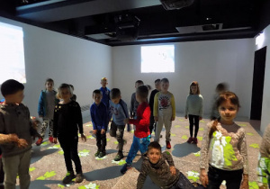 Dzieci pozują w sali z oświetloną podłogą i ścianami.