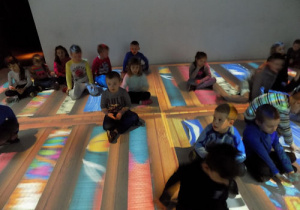 Dzieci siedzą na kolorowo oświetlonej podłodze.