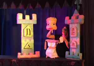 Aktorka trzyma kukiełkę na tle zamku