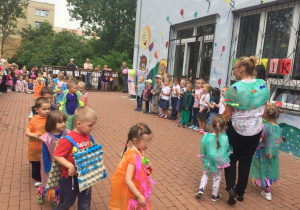 Przebrane w kolorowe stroje dzieci stoją z nauczycielkami w półkolu