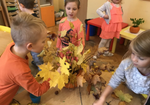 Do wcześniej wypełnionej dyni słoikiem z woda i kasztanami dzieci układały liście