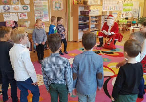 Dzieci stoją w kole z Mikołajem.