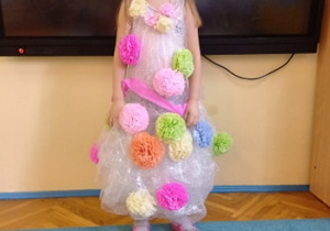 Dziewczynka w sukience z foli bąbelkowej ozdobionej kwiatami z bibuły.