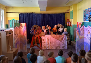 Dzieci oglądają przedstawienie. Na scenie aktorzy z lalkami.