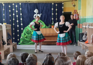 Dzieci oglądają występ taneczny, na scenie znajdują się dwie tancerki.