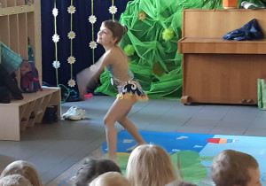 Dziewczynka tańczy na dywanie. Dzieci oglądają jej występ.
