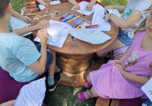 Dzieci przy stoliku w ogrodzie kolorują obrazki.