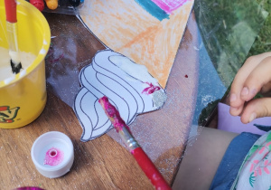 Dziewczynka maluje pokolorowanego loda klejem brokatowym.