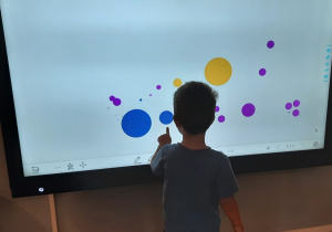 Chłopiec rysuje na monitorze multimedialnym kolorowe kropki