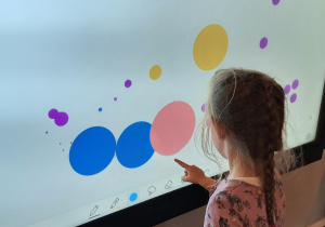 Dziewczynka na monitorze multimedialnym rysuje kolorowe kropki