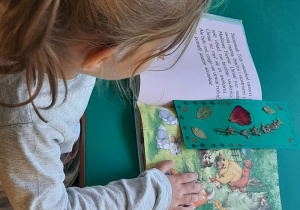 Dziewczynka ogląda obrazki w książce, w której znajduje się wykonana przez dzieci zakładka