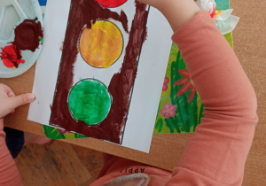 Dziecko koloruje farbami ilustrację sygnalizatora.