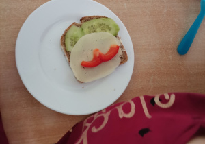 Na talerzu leży kanapka, na której dzieci stworzyły uśmiech z ogórków i papryki.