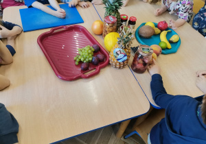 Dzieci siedzą przy stoliku na którym leżą owoce oraz przetwory z owoców.