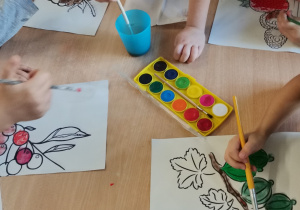 Dzieci siedzą przy stoliku - malują farbami owoce.