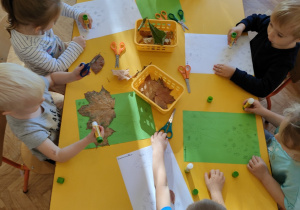 Dzieci przy stoliku wyklejają obrazek liśćmi