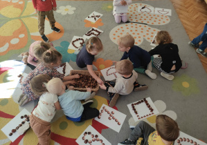 Dzieci siedzą na dywanie i układają z kasztanów liczby i wzory