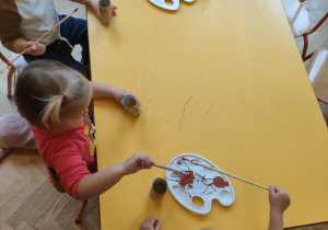 Dzieci malują farbami przy stoliku rolki po papierze toaletowym na kolor brązowy