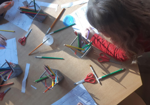 Dzieci siedzą przy stoliku i kolorują kredkami karty pracy przedstawiające połówki śliwek.